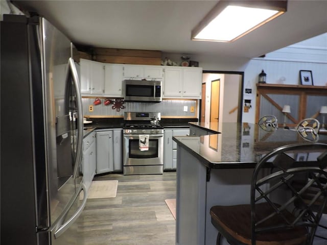 1820 Oak Grove Rd, Van Buren, AR 72956 - kitchen featuring light wood finished floors, white cabinetry, appliances with stainless steel finishes, a kitchen bar, and dark countertops