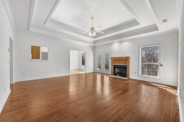 unfurnished living room featuring a tray ceiling, a fireplace with flush hearth, ceiling fan with notable chandelier, and hardwood / wood-style flooring