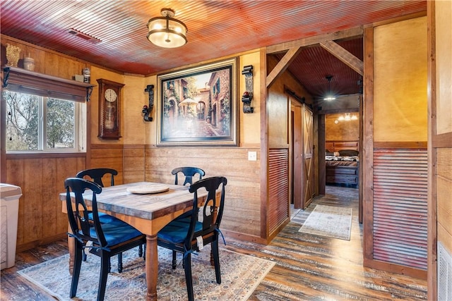 dining area featuring a barn door, wooden walls, wood finished floors, and wooden ceiling