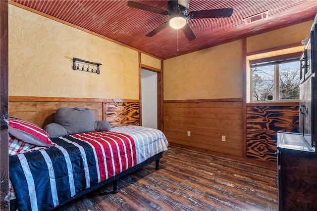 bedroom with visible vents, wooden walls, wainscoting, wood finished floors, and a ceiling fan