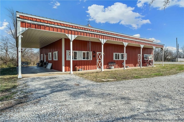 view of side of home featuring an exterior structure, board and batten siding, gravel driveway, metal roof, and an outbuilding