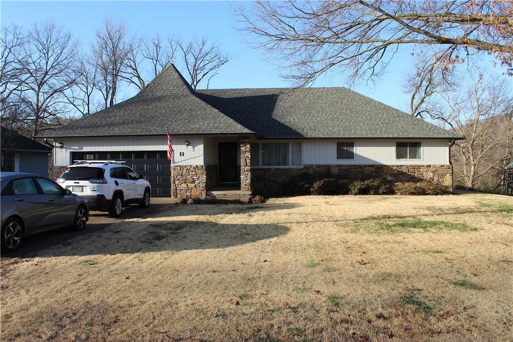 ranch-style house featuring an attached garage, stone siding, driveway, and roof with shingles