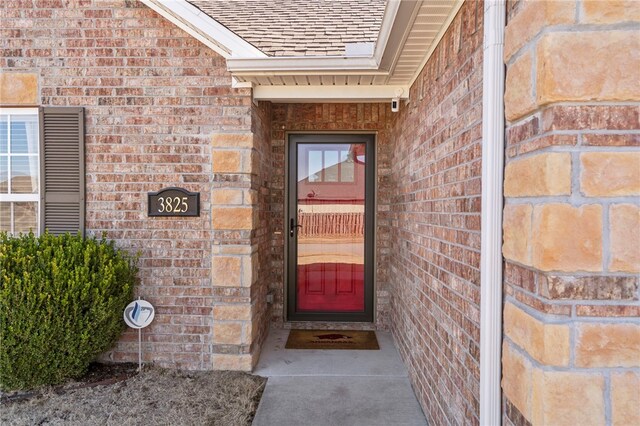 view of exterior entry featuring brick siding and roof with shingles