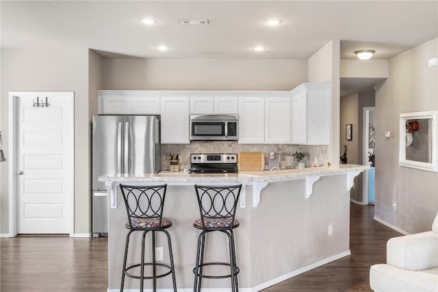 kitchen with dark wood-style flooring, white cabinets, appliances with stainless steel finishes, a kitchen bar, and backsplash