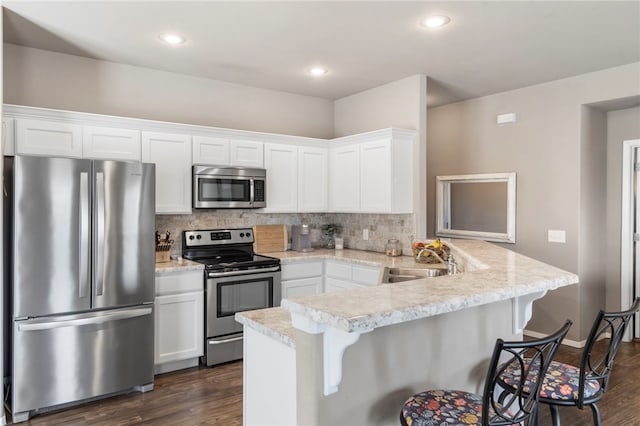 kitchen featuring a kitchen bar, a peninsula, appliances with stainless steel finishes, and a sink