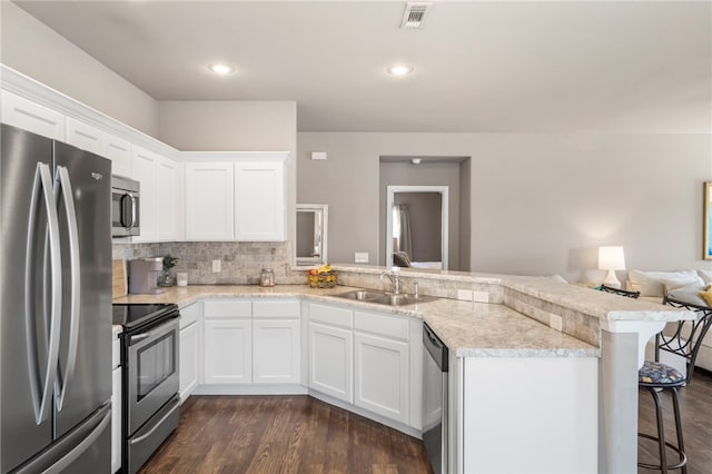 kitchen featuring visible vents, a peninsula, a sink, stainless steel appliances, and a kitchen breakfast bar