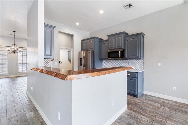 kitchen with baseboards, a peninsula, light wood-style flooring, stainless steel appliances, and backsplash