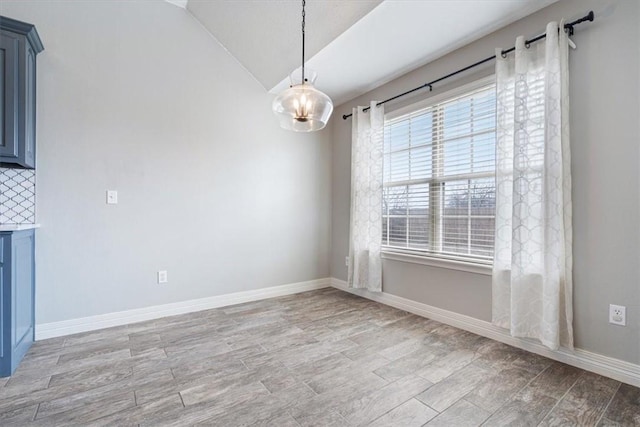 unfurnished dining area featuring baseboards, light wood-type flooring, and lofted ceiling