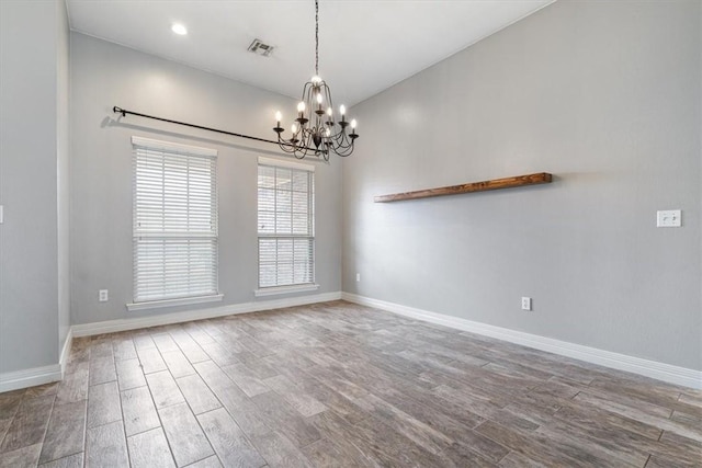 empty room featuring visible vents, baseboards, a notable chandelier, and wood finished floors