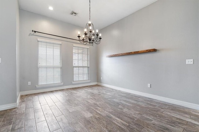 spare room featuring a chandelier, wood finished floors, visible vents, and baseboards