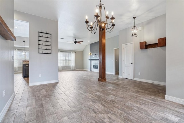 unfurnished living room featuring lofted ceiling, ceiling fan with notable chandelier, wood finished floors, a large fireplace, and baseboards