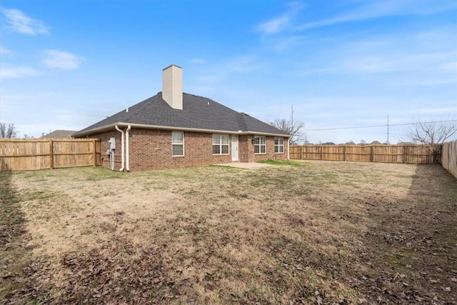 rear view of property with brick siding, a lawn, a chimney, and a fenced backyard