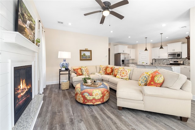 living room featuring wood finished floors, visible vents, baseboards, recessed lighting, and a glass covered fireplace