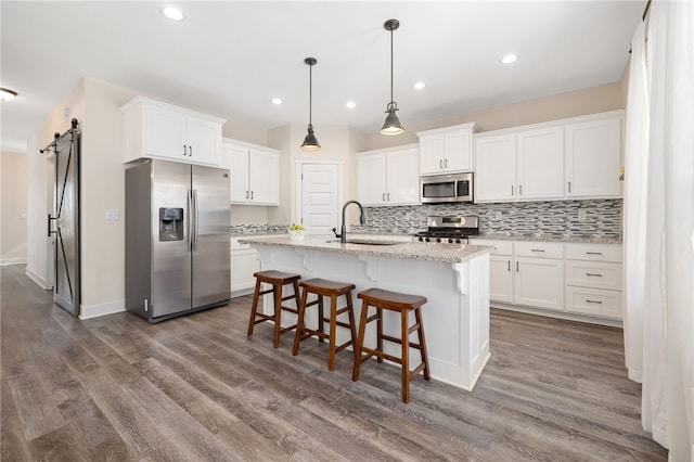 kitchen with a barn door, backsplash, appliances with stainless steel finishes, and white cabinets