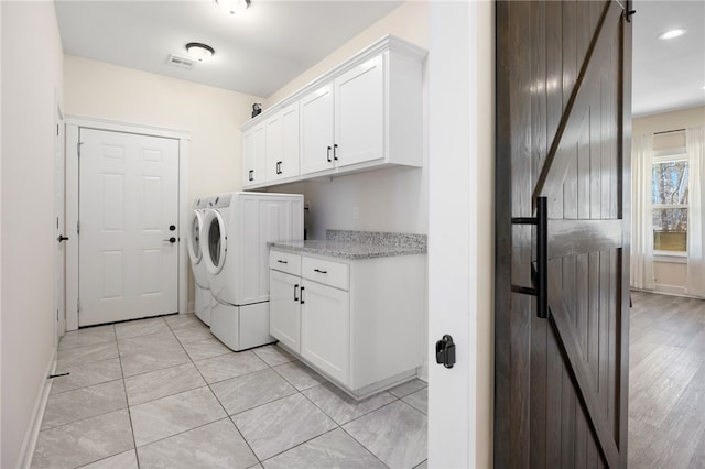 laundry area featuring visible vents, washer and clothes dryer, a barn door, cabinet space, and baseboards