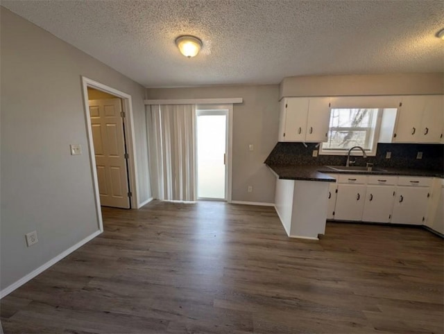 kitchen featuring dark countertops, white cabinets, dark wood finished floors, and a sink