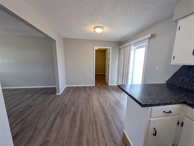 kitchen with dark countertops, baseboards, a peninsula, wood finished floors, and white cabinets