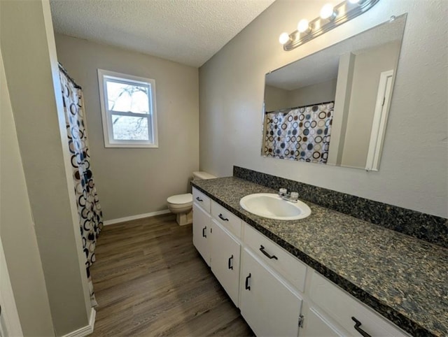 full bathroom with vanity, wood finished floors, baseboards, a textured ceiling, and toilet