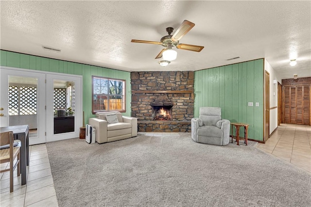 tiled living room with visible vents, a textured ceiling, a stone fireplace, and carpet