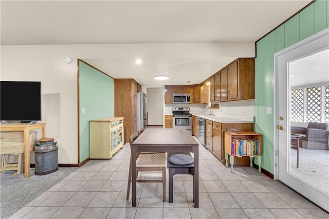 kitchen with brown cabinetry, light tile patterned floors, stainless steel appliances, and light countertops