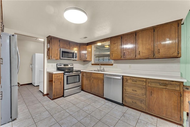 kitchen featuring visible vents, a sink, stainless steel appliances, brown cabinetry, and light countertops