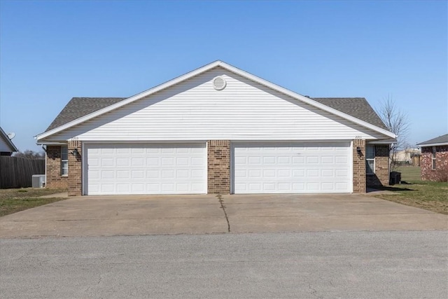 garage with central AC unit, concrete driveway, and fence