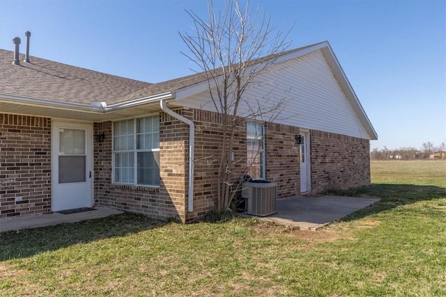 view of property exterior with a patio, central AC, a yard, a shingled roof, and brick siding