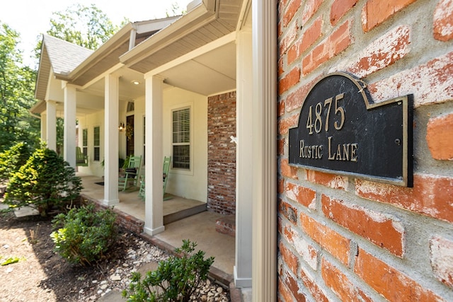 view of exterior entry with brick siding, covered porch, and a shingled roof