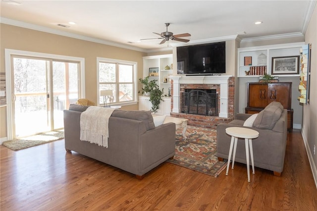 living room featuring visible vents, crown molding, a fireplace, wood finished floors, and a ceiling fan