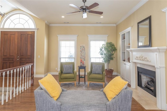 living area featuring a tiled fireplace, built in features, baseboards, and wood finished floors