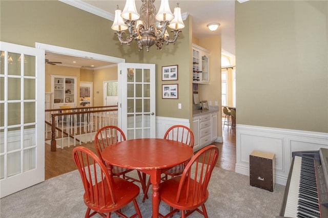 carpeted dining area featuring wainscoting, french doors, and crown molding