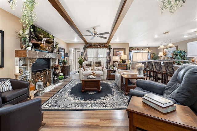 living room with beamed ceiling, a fireplace, a ceiling fan, and wood finished floors