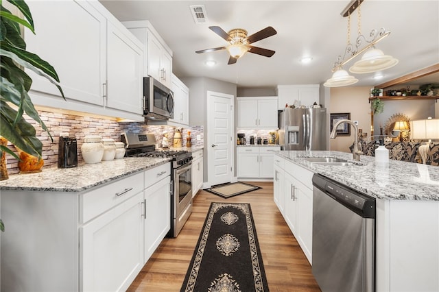 kitchen with visible vents, a sink, stainless steel appliances, light wood finished floors, and decorative backsplash