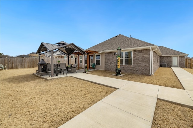 view of front facade featuring brick siding, roof with shingles, a gazebo, a fenced backyard, and a patio area