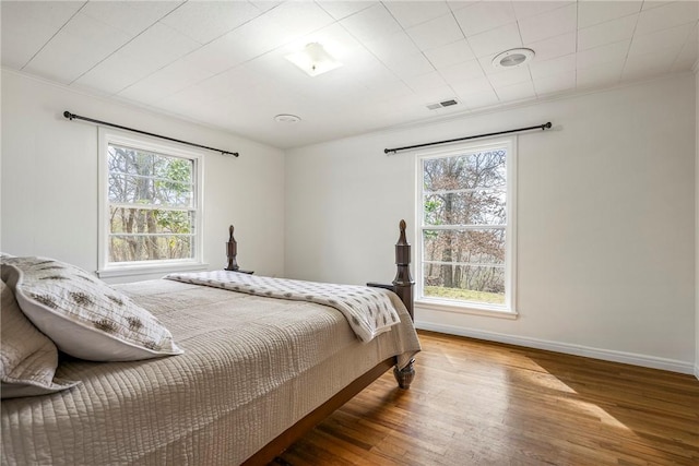 bedroom featuring baseboards, multiple windows, wood finished floors, and ornamental molding