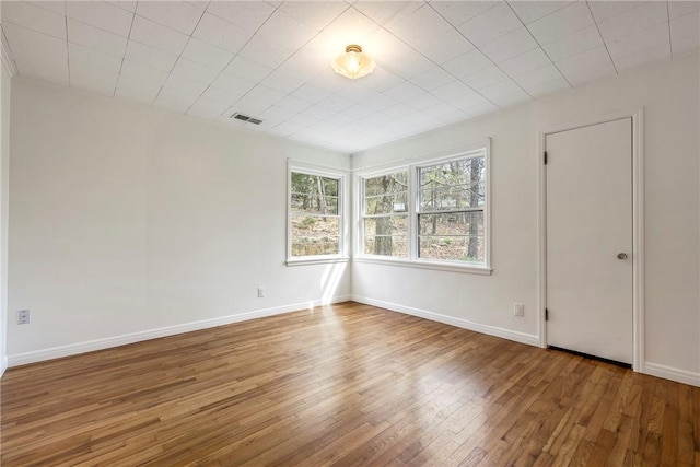 unfurnished room featuring visible vents, wood-type flooring, and baseboards