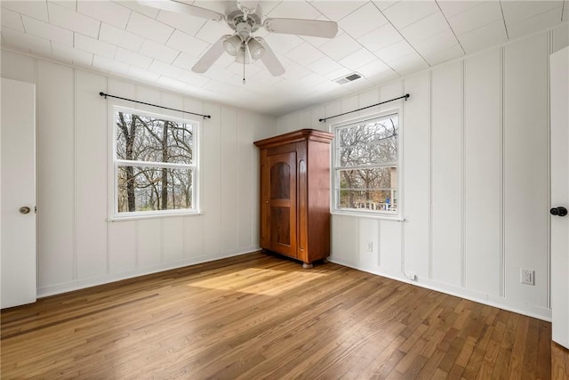 unfurnished bedroom with a decorative wall, a ceiling fan, visible vents, and wood-type flooring