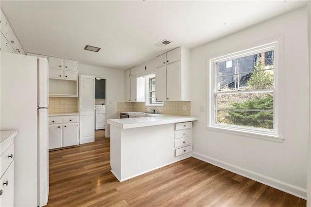 kitchen with light wood-type flooring, washer / clothes dryer, backsplash, freestanding refrigerator, and a peninsula