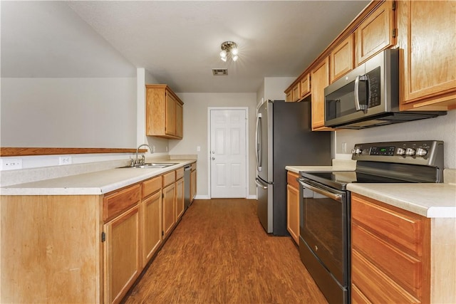 kitchen featuring visible vents, dark wood finished floors, a peninsula, a sink, and stainless steel appliances