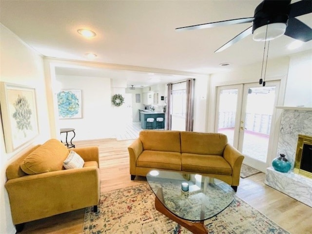 living area with a premium fireplace, wood finished floors, a ceiling fan, and french doors