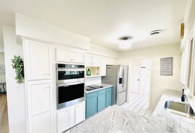 kitchen with visible vents, stainless steel appliances, white cabinetry, blue cabinets, and a sink