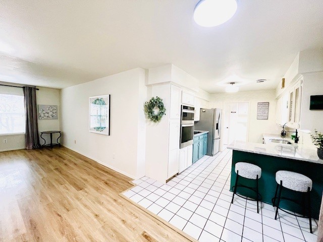 kitchen with light wood-type flooring, light countertops, white cabinets, stainless steel fridge, and a sink