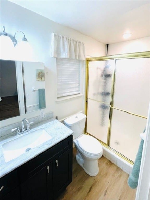 bathroom with vanity, toilet, wood finished floors, and a stall shower