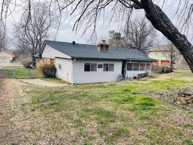 back of house featuring fence, a yard, roof with shingles, a sunroom, and a chimney