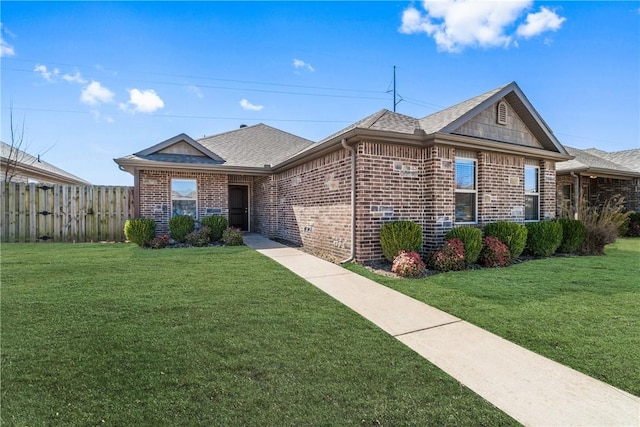 view of front of house with brick siding, roof with shingles, a front lawn, and fence