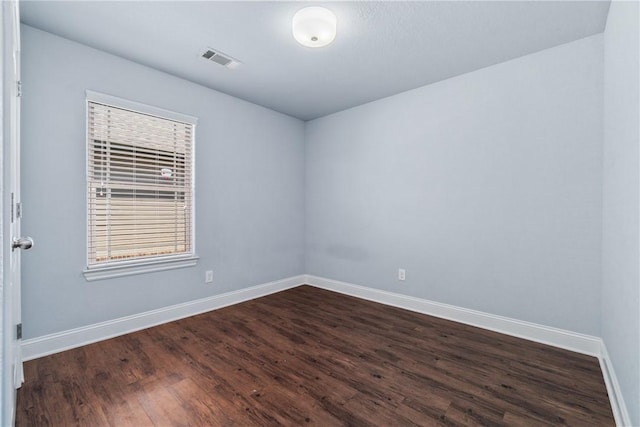 unfurnished room featuring dark wood finished floors, visible vents, and baseboards