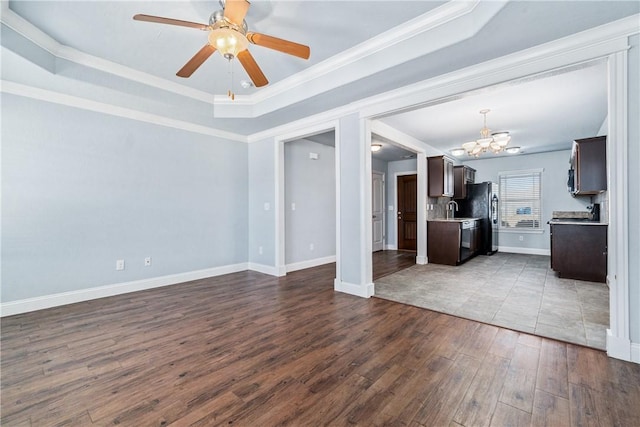 unfurnished living room with baseboards, a tray ceiling, dark wood-type flooring, crown molding, and ceiling fan with notable chandelier