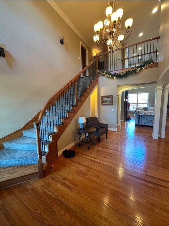 staircase featuring wood finished floors, a high ceiling, arched walkways, ornamental molding, and a chandelier