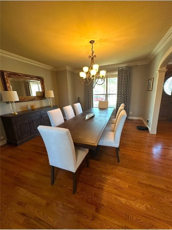 dining space with baseboards, ornamental molding, wood finished floors, arched walkways, and a notable chandelier