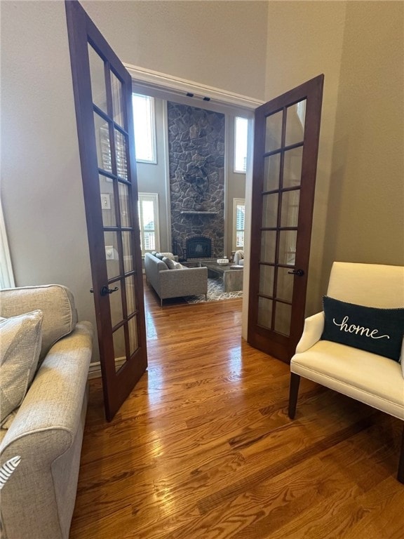 living area featuring a stone fireplace, french doors, a high ceiling, and wood finished floors